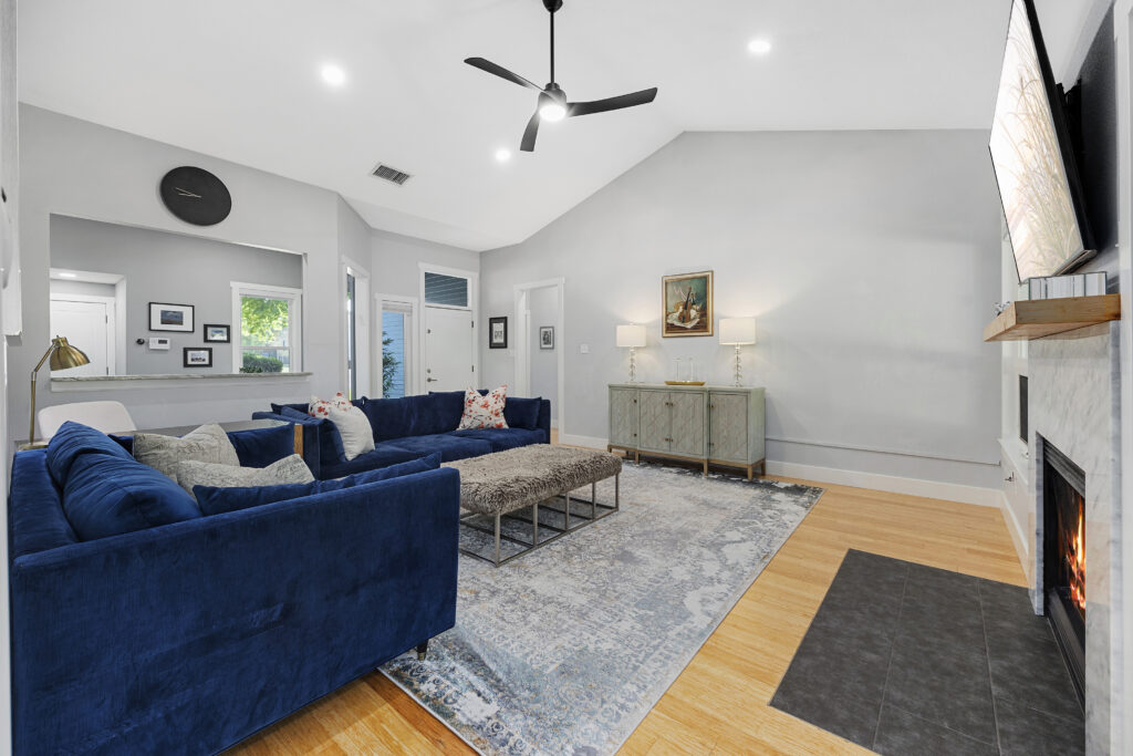 Open-concept living room with a spacious layout and vaulted ceiling, neutral tones, granite fireplace, and modern furniture.