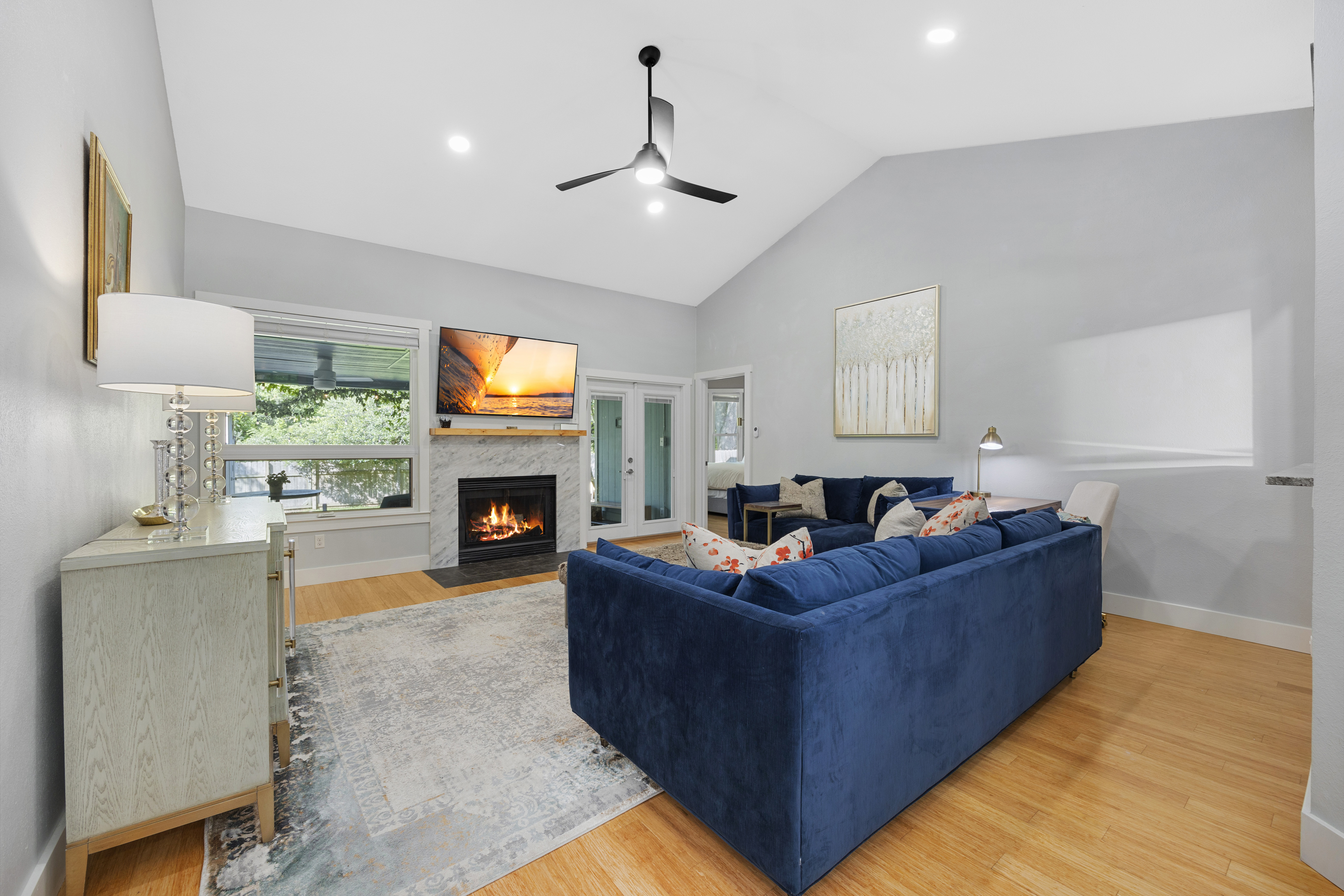 Open-concept living room with a spacious layout and vaulted ceiling, neutral tones, granite fireplace, and modern furniture.