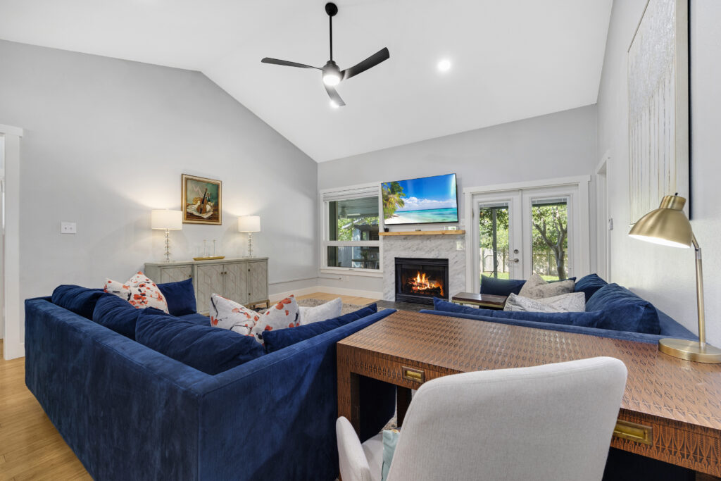 Open-concept living room with a spacious layout and vaulted ceiling, neutral tones, granite fireplace, work-from-home space, and modern furniture.