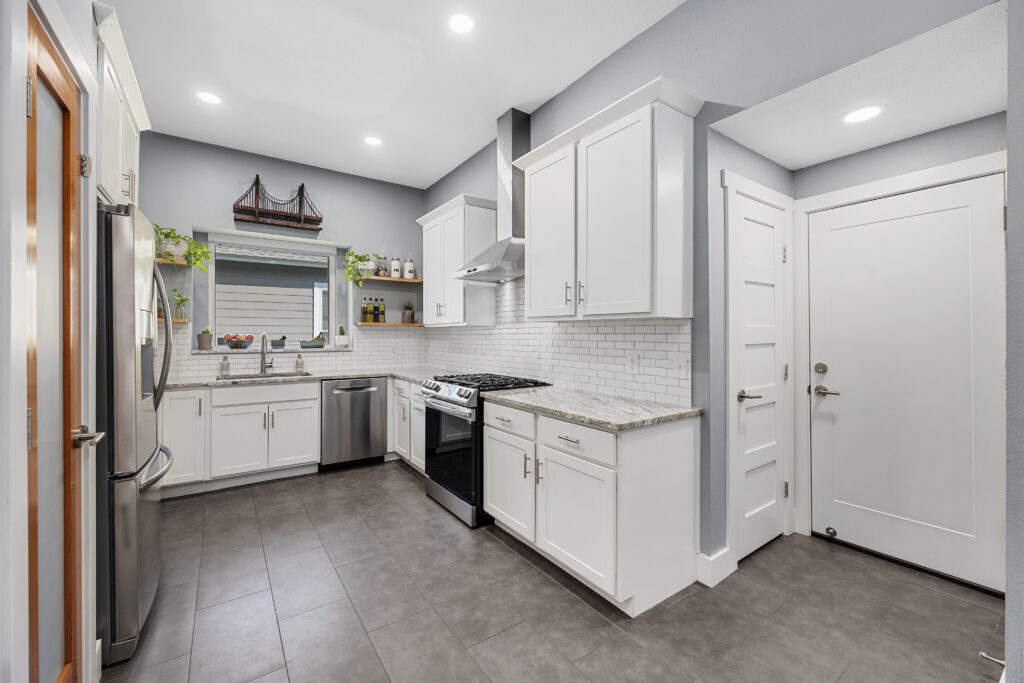 White modern kitchen with granite countertops, shaker cabinets, porcelain tile floors and stainless steel appliances.