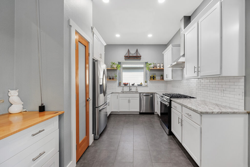 White modern kitchen with granite countertops, shaker cabinets, porcelain tile floors and stainless steel appliances.