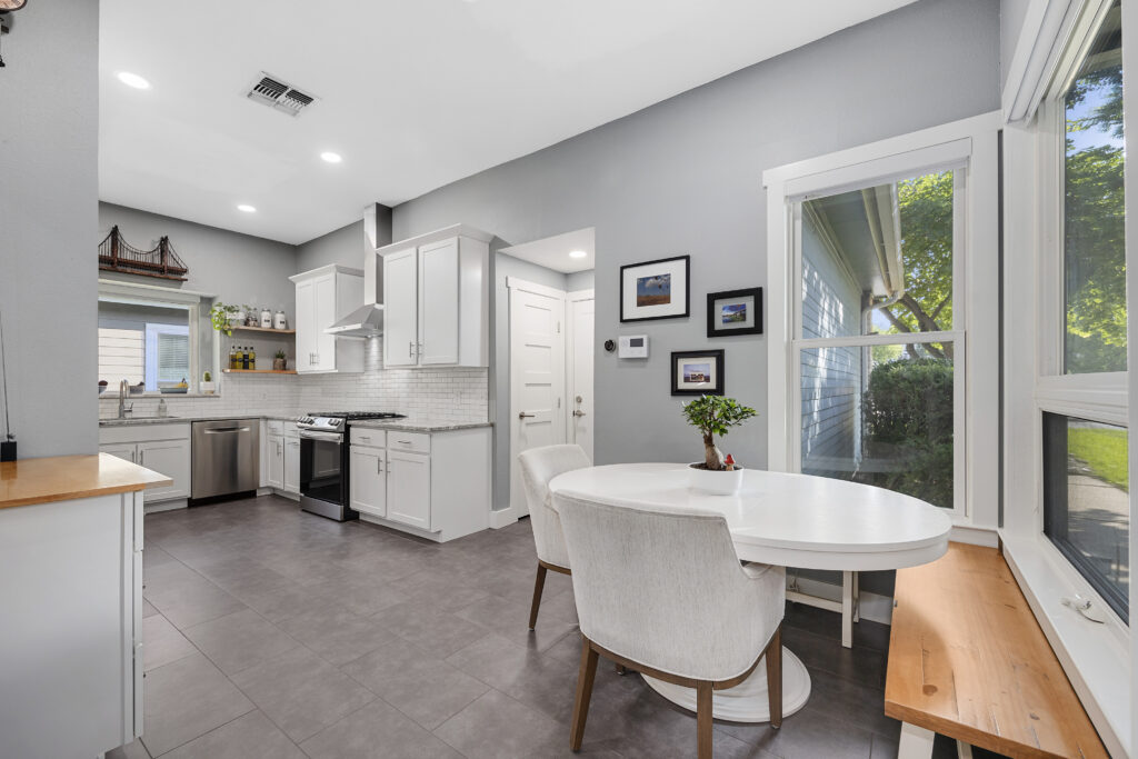 White modern kitchen with granite countertops, shaker cabinets, porcelain tile floors, stainless steel appliances and an eat-in kitchen area.