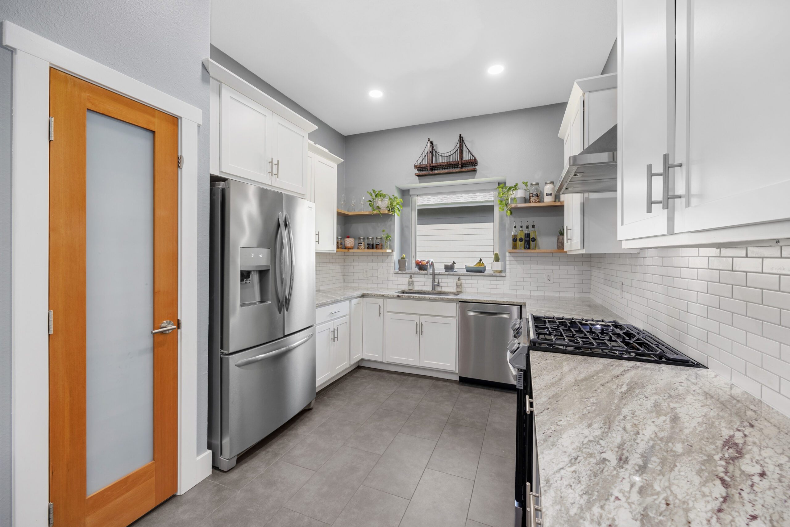 White modern kitchen with granite countertops, shaker cabinets, porcelain tile floors and stainless steel appliances.