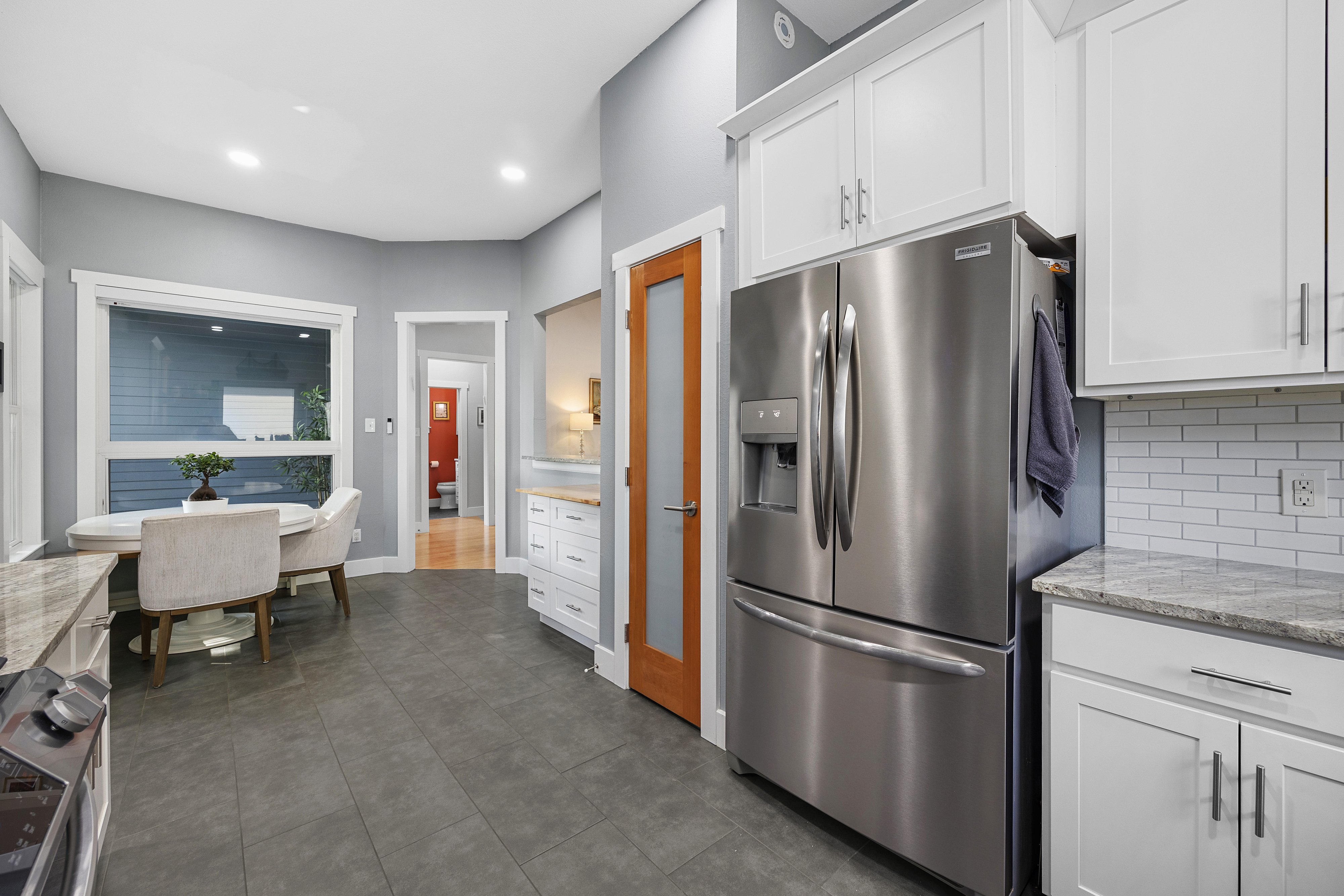 White modern kitchen with granite countertops, shaker cabinets, porcelain tile floors and stainless steel appliances.