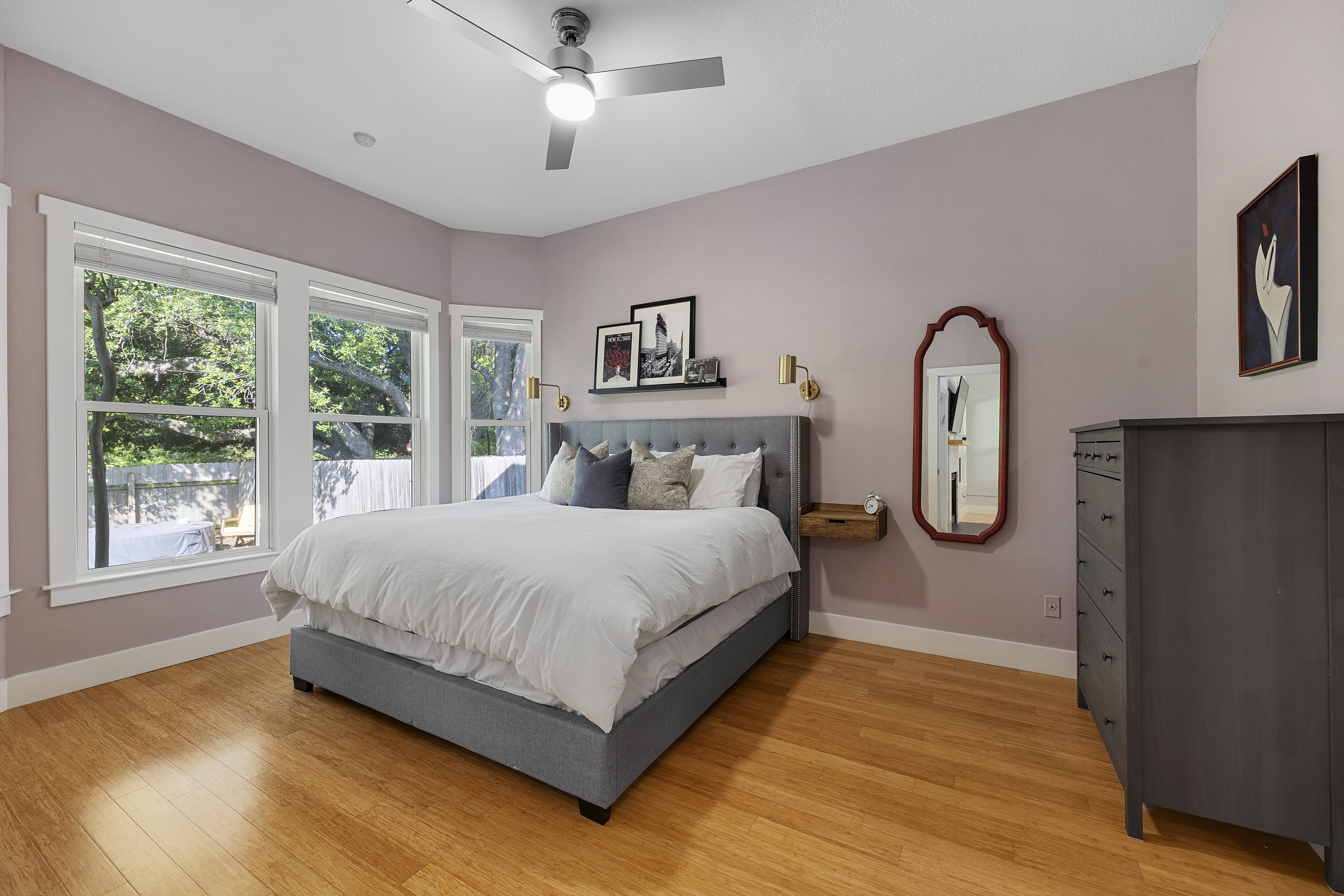 Master bedroom with mauve walls, a spacious layout, a king bed, floating nightstands, window trim, large windows, tall ceilings, and a dresser.