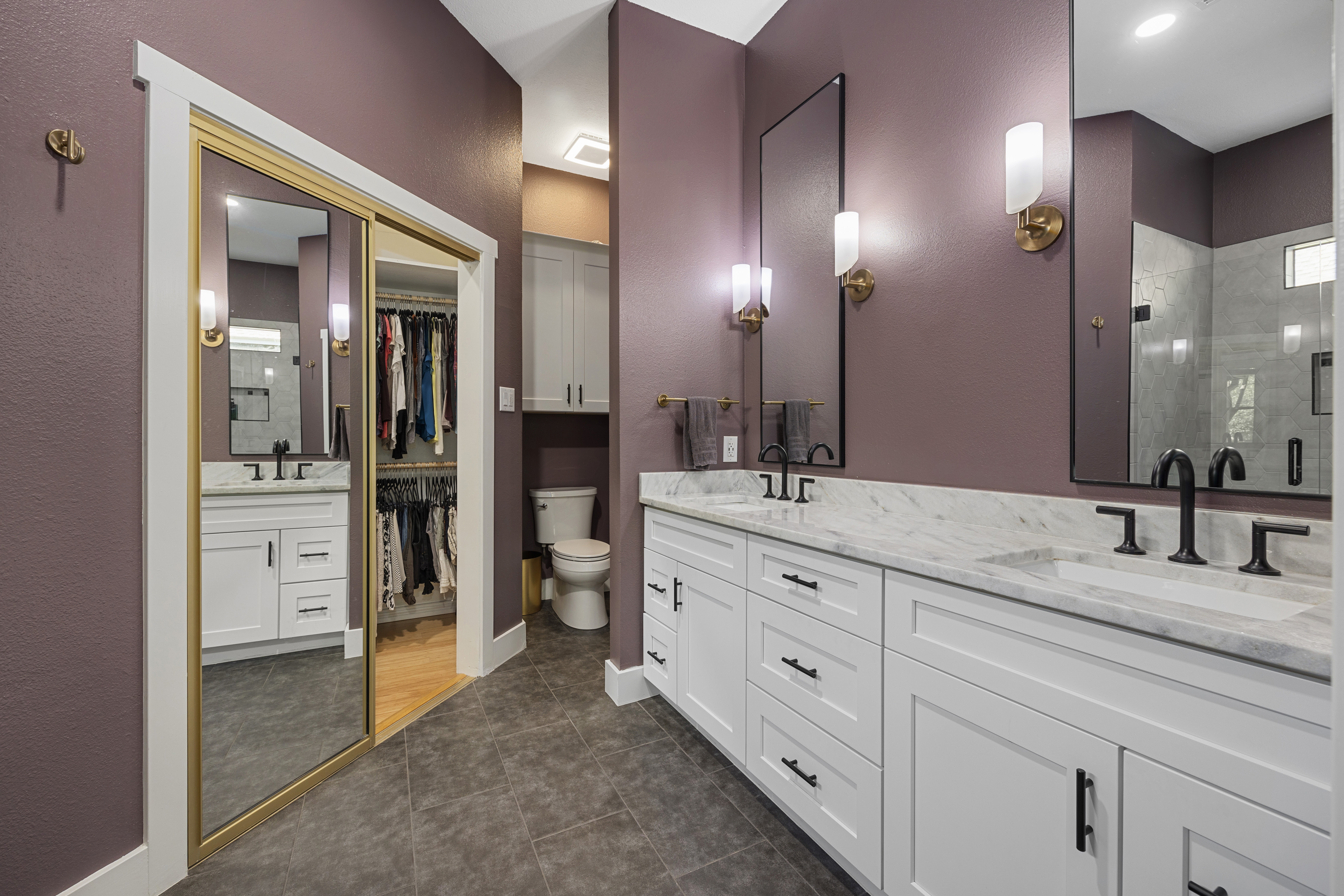 Modern master bathroom with a large walk-in glass shower with hexagon wall tiles, white double vanity cabinets, granite countertops, dark purple walls, and designer black fixtures.