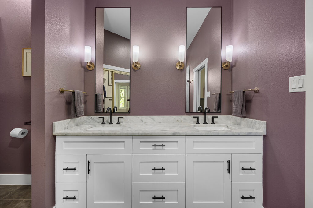 Modern master bathroom with a large walk-in glass shower with hexagon wall tiles, white double vanity cabinets, granite countertops, dark purple walls, and designer black fixtures.