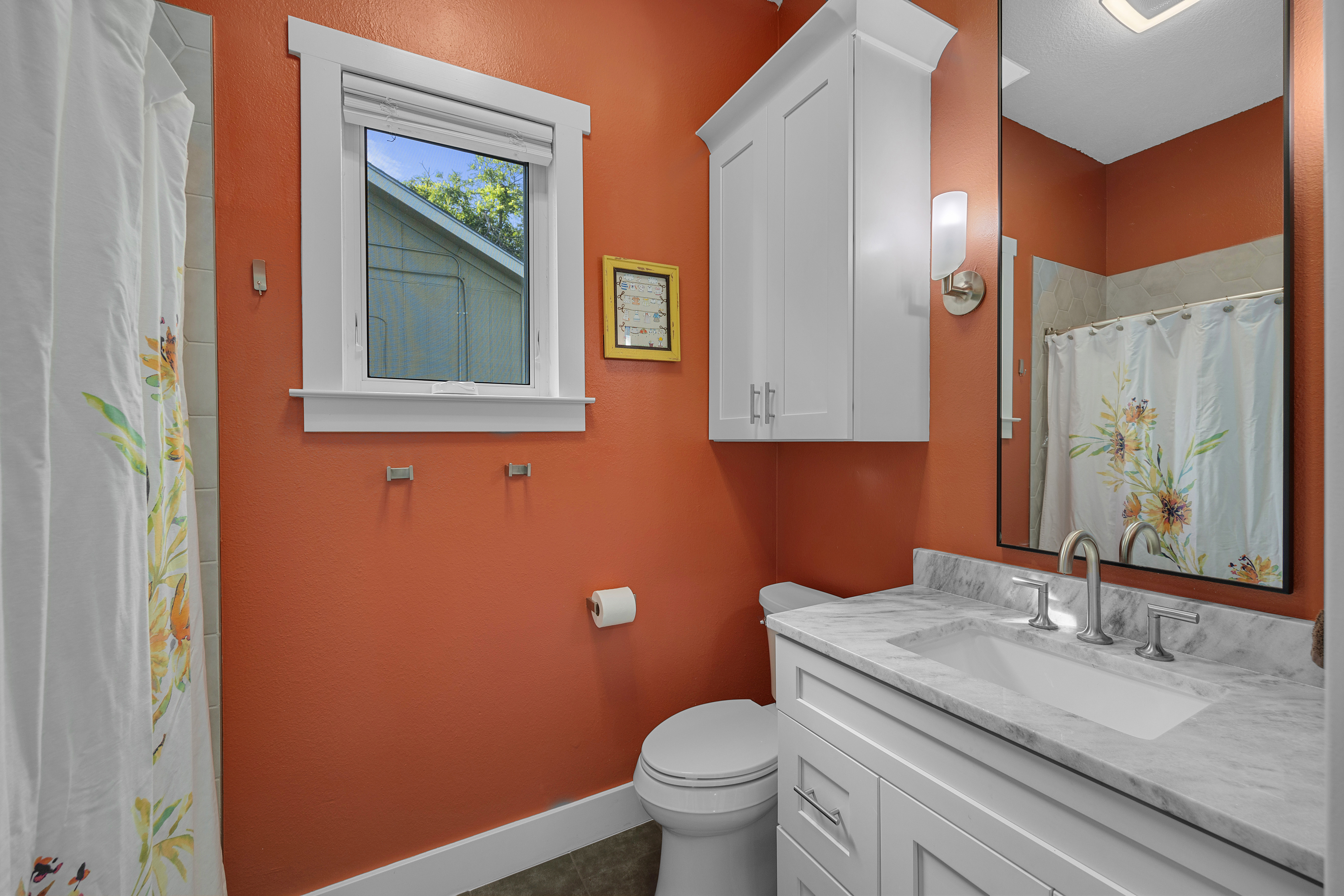 Guest bathroom with terracotta walls, a single white vanity with granite countertops, a tub-shower combo, hexagon wall tiles, and patterned tile flooring.