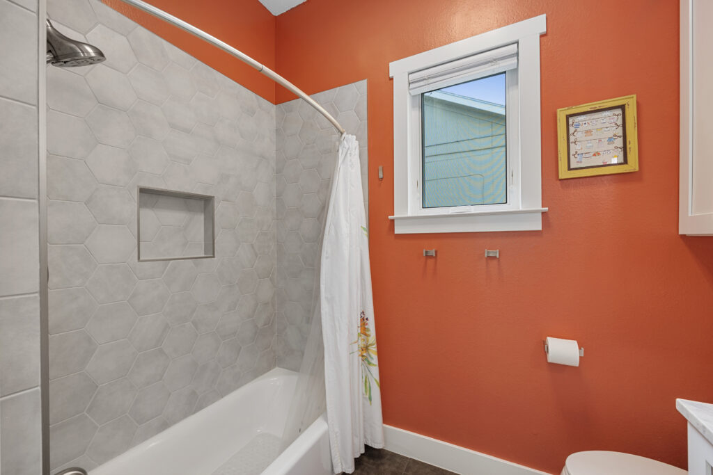 Guest bathroom with terracotta walls, a single white vanity with granite countertops, a tub-shower combo, hexagon wall tiles, and patterned tile flooring.